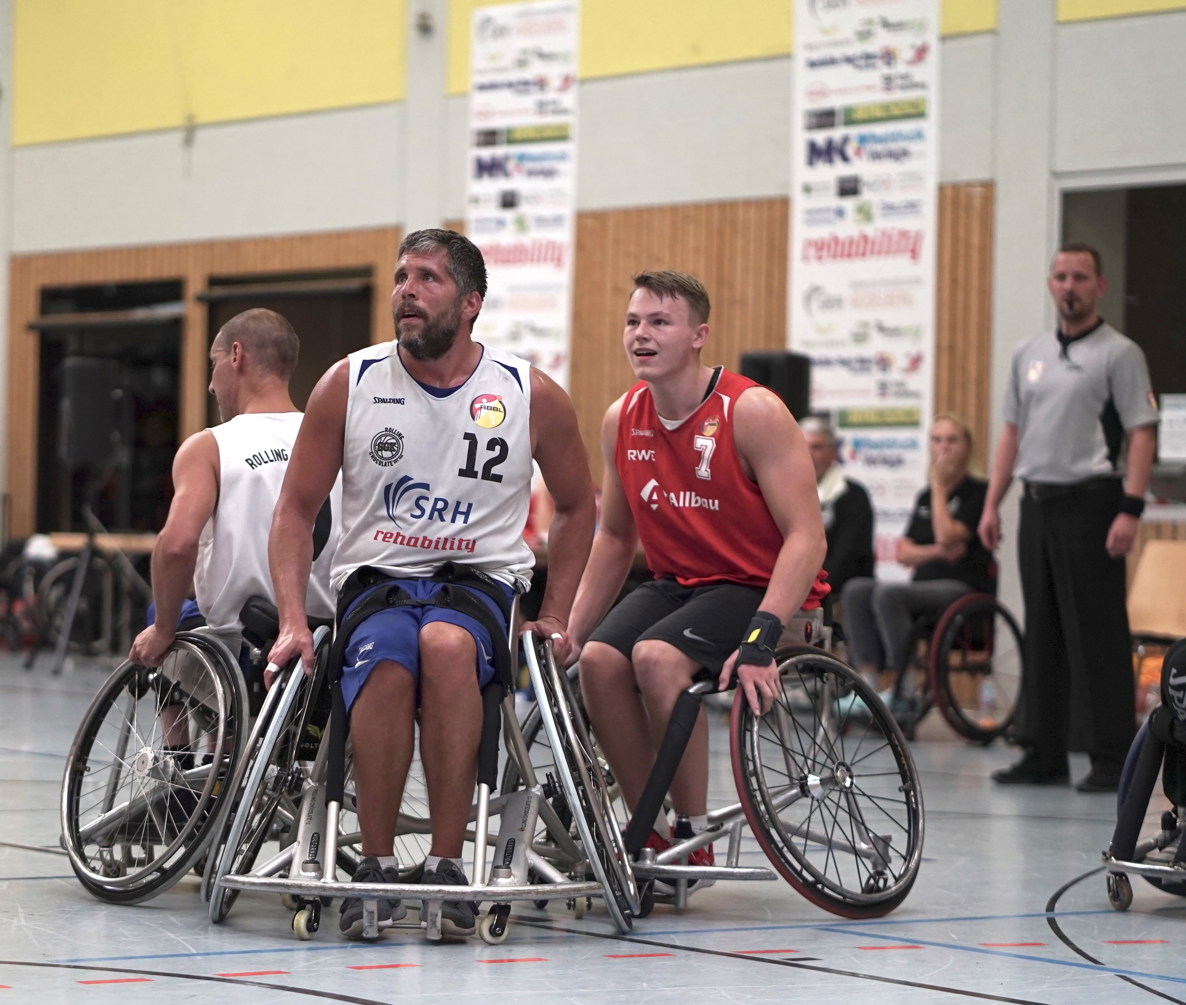 Zwei Rollstuhlbasketballer schauen gebannt auf den Ball, der auf der anderen Seite des Spielfelds ist.